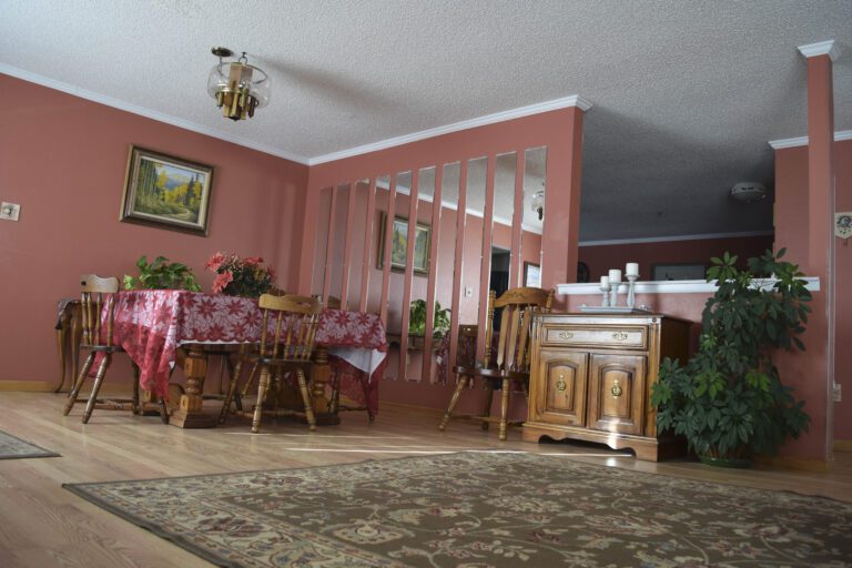 Dinging area with table and chairs. Rose colored walls, several vertical mirrors on the wall to the right, back wall has a painting, celling painted white. Wood laminate floors with area rug.