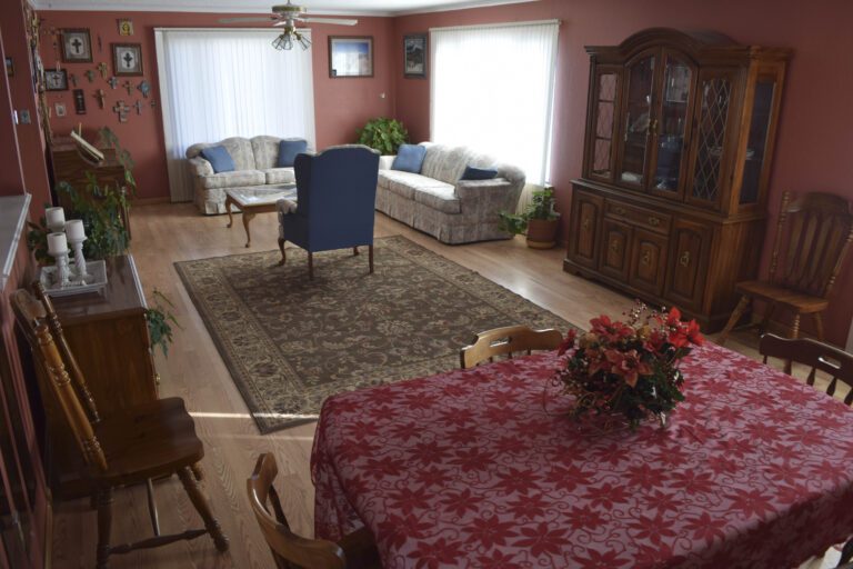 Dining table with flowers on top. Living room to include blue chair, coffee table, love seat, couch, and ceiling fan.