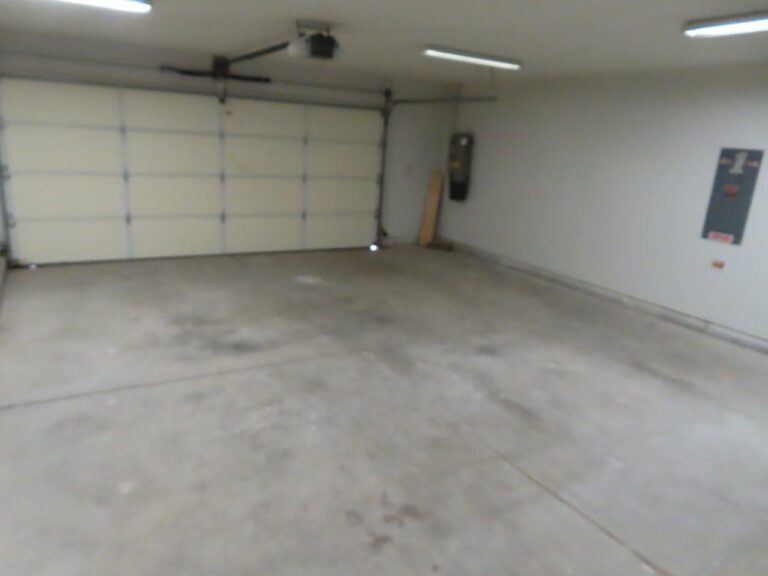 A well-lit, large two car attached garage with a concrete floor. Garage door opener overhead.