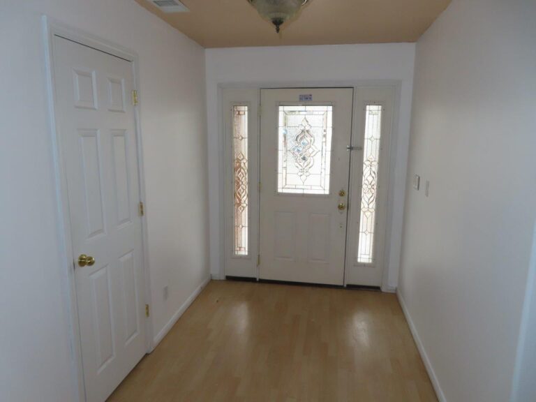 Main entranceway with view of the front door with tempered glass allowing natural light in. Beige laminate wood flooring. Hall closet door to the left, wall to the right.